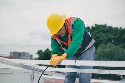 A construction worker with safety gear installing solar panels on a sunny day.